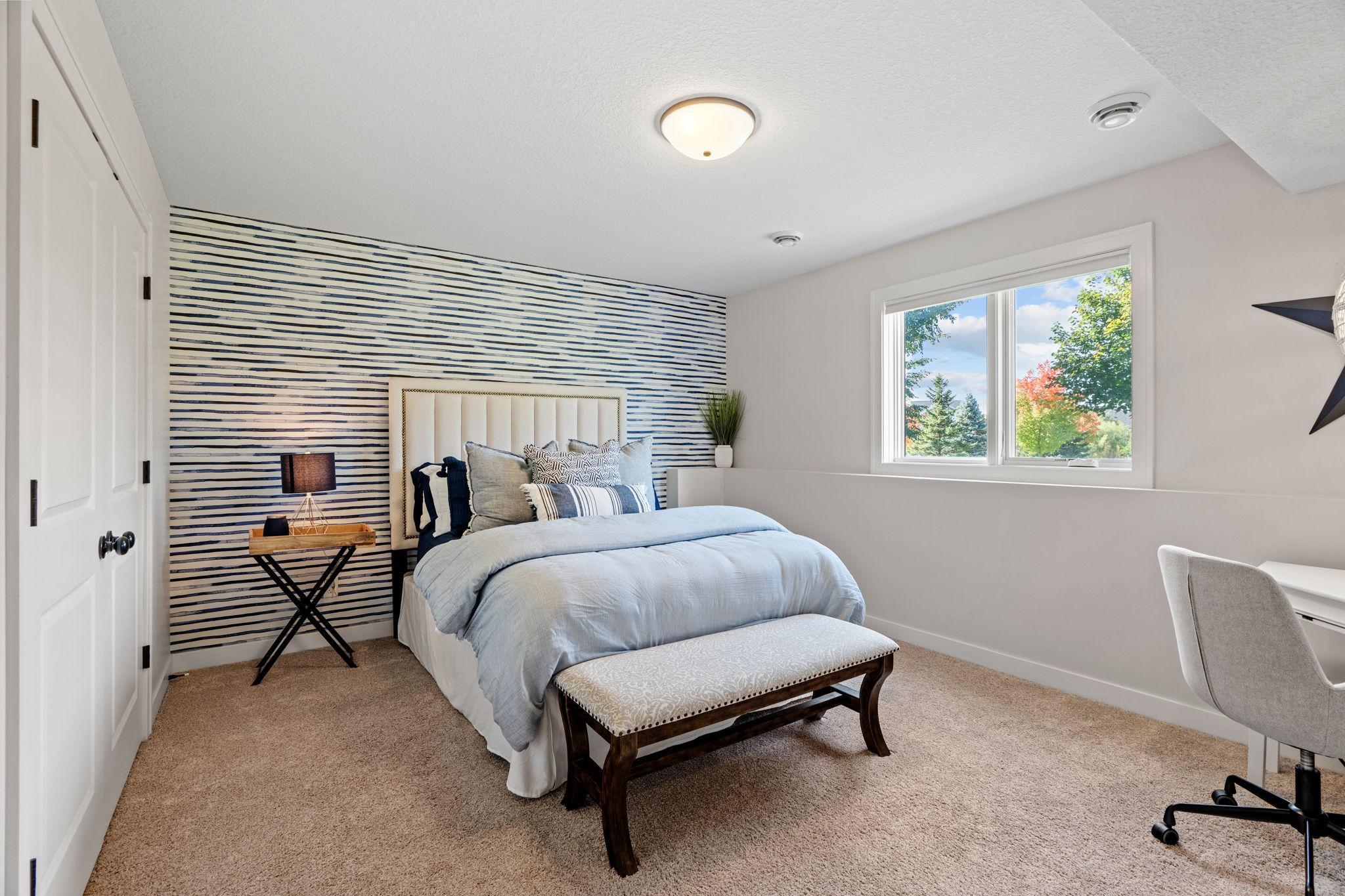 Staged bedroom with a blue-and-white striped accent wall, pale blue bedding, and a bright window.