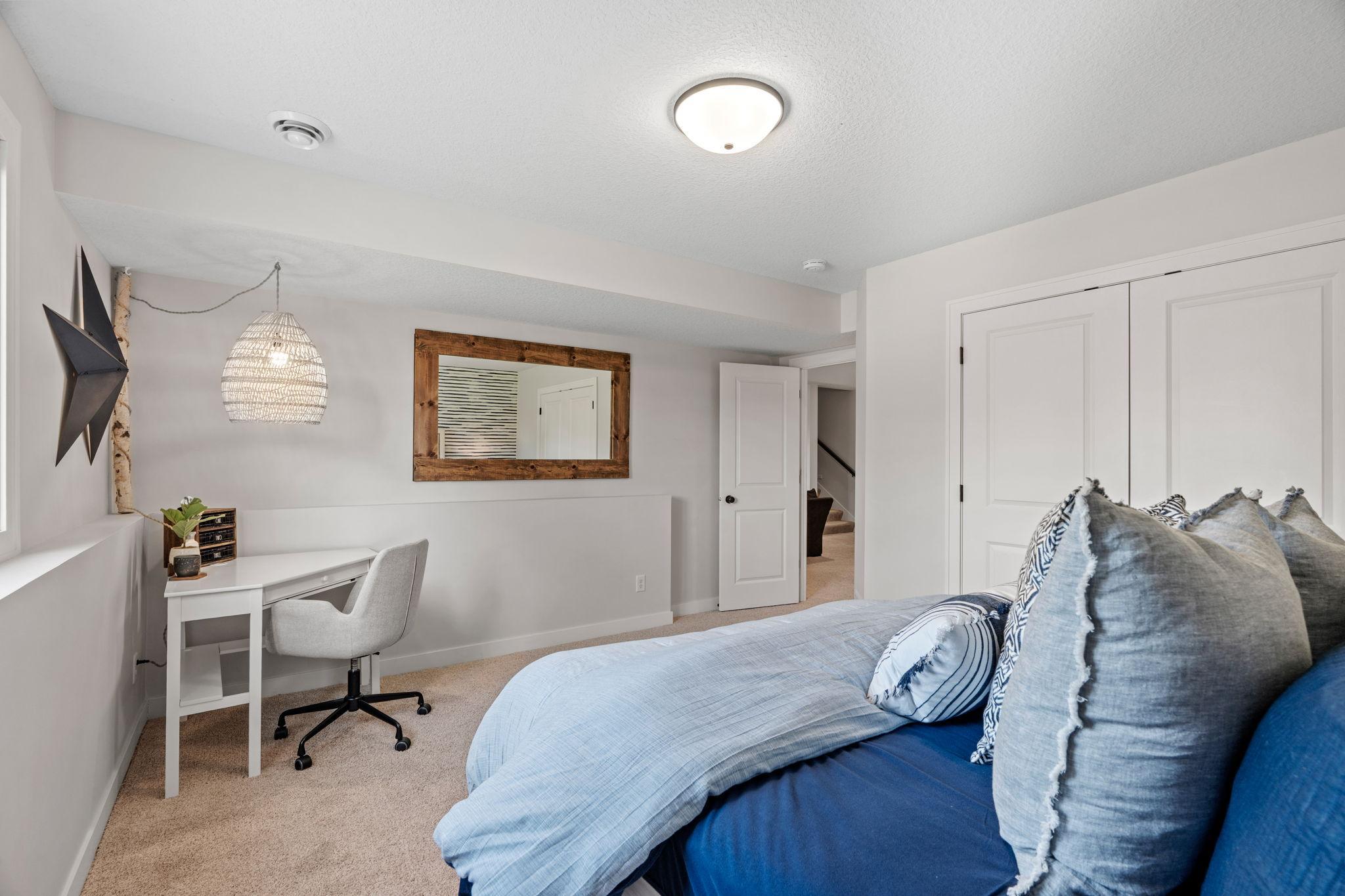 Bedroom with a blue bed, gray pillows, and a small white desk beneath a woven pendant light.