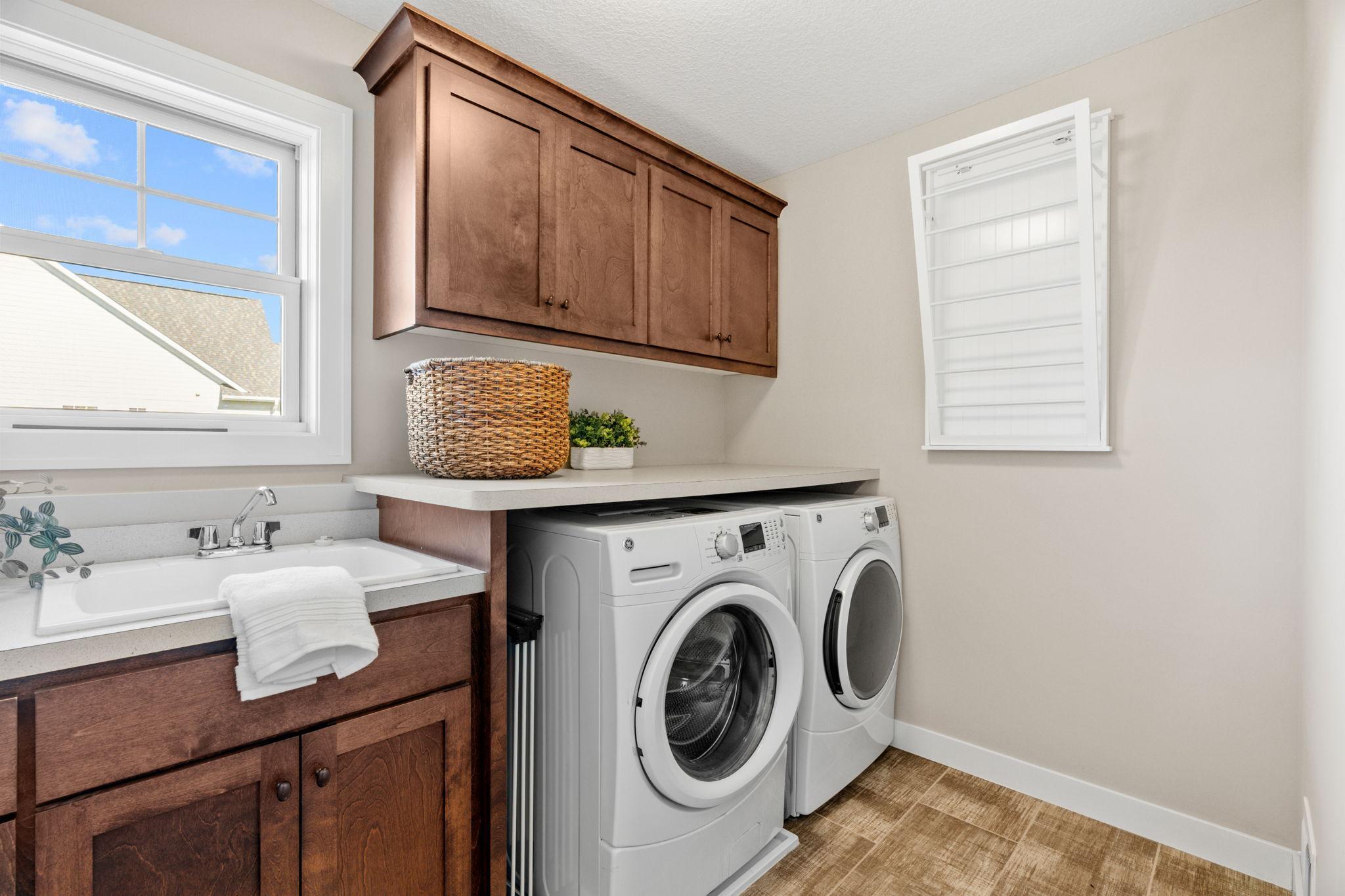 Laundry room with front-loading washer and dryer, dark wood cabinets, and a utility sink.