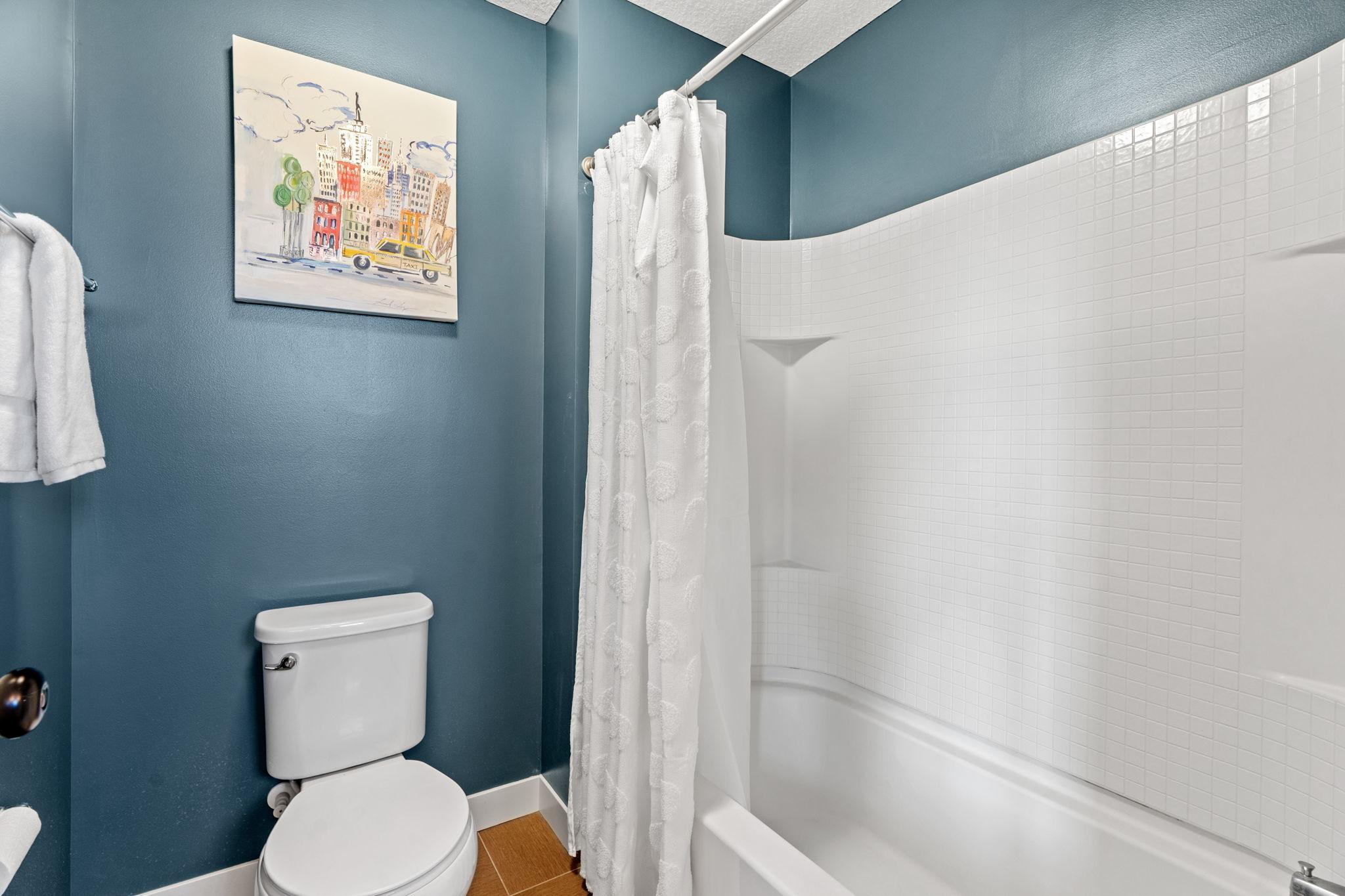 Bathroom with teal walls, a white toilet, and a tiled bathtub behind a shower curtain.
