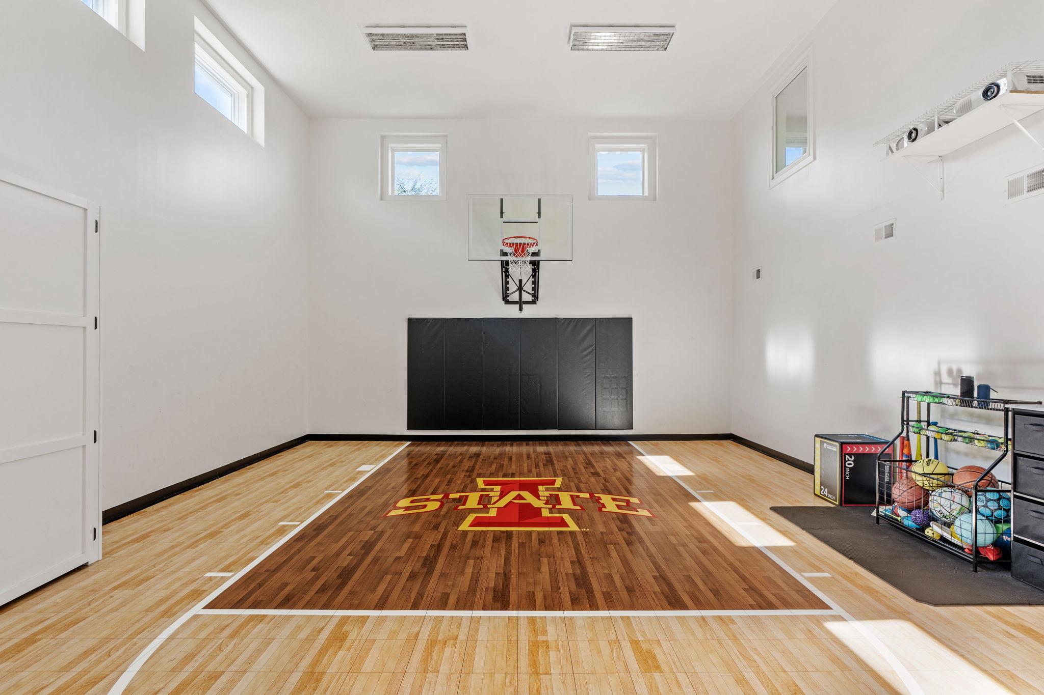 Indoor basketball court with polished wood flooring, a STATE center-court logo, hoop, and ball rack.