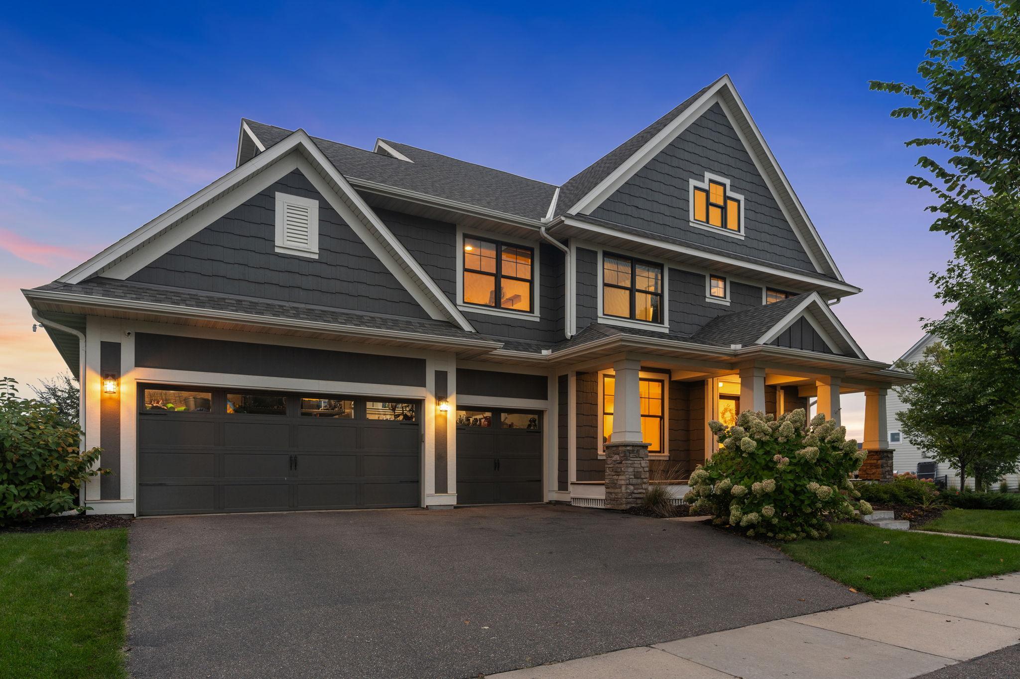 Dark-gray gabled home with a two-car garage and warmly lit windows at dusk.