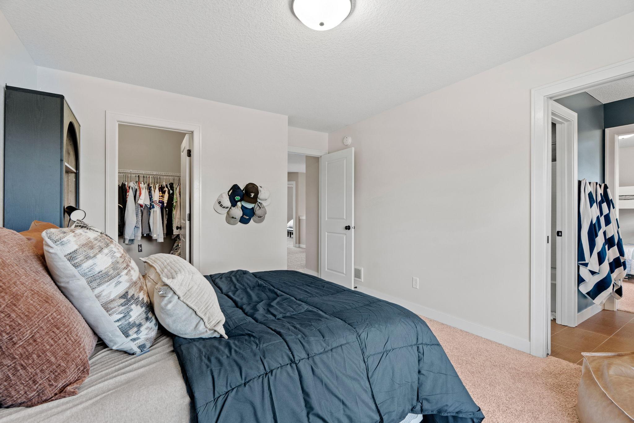 Bedroom with a navy-covered bed, open clothes closet, and hats displayed on the wall.