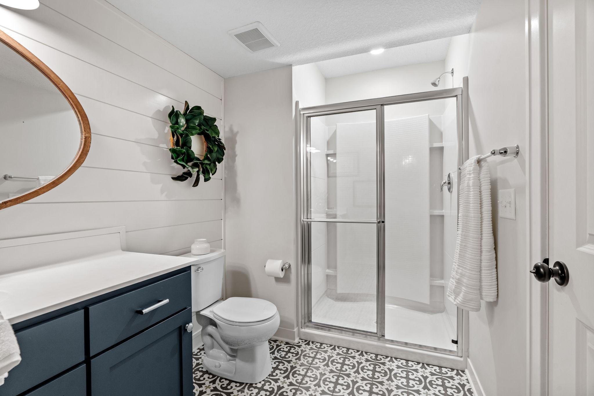 Bathroom with a dark blue vanity, glass shower, and patterned black-and-white tile floor.