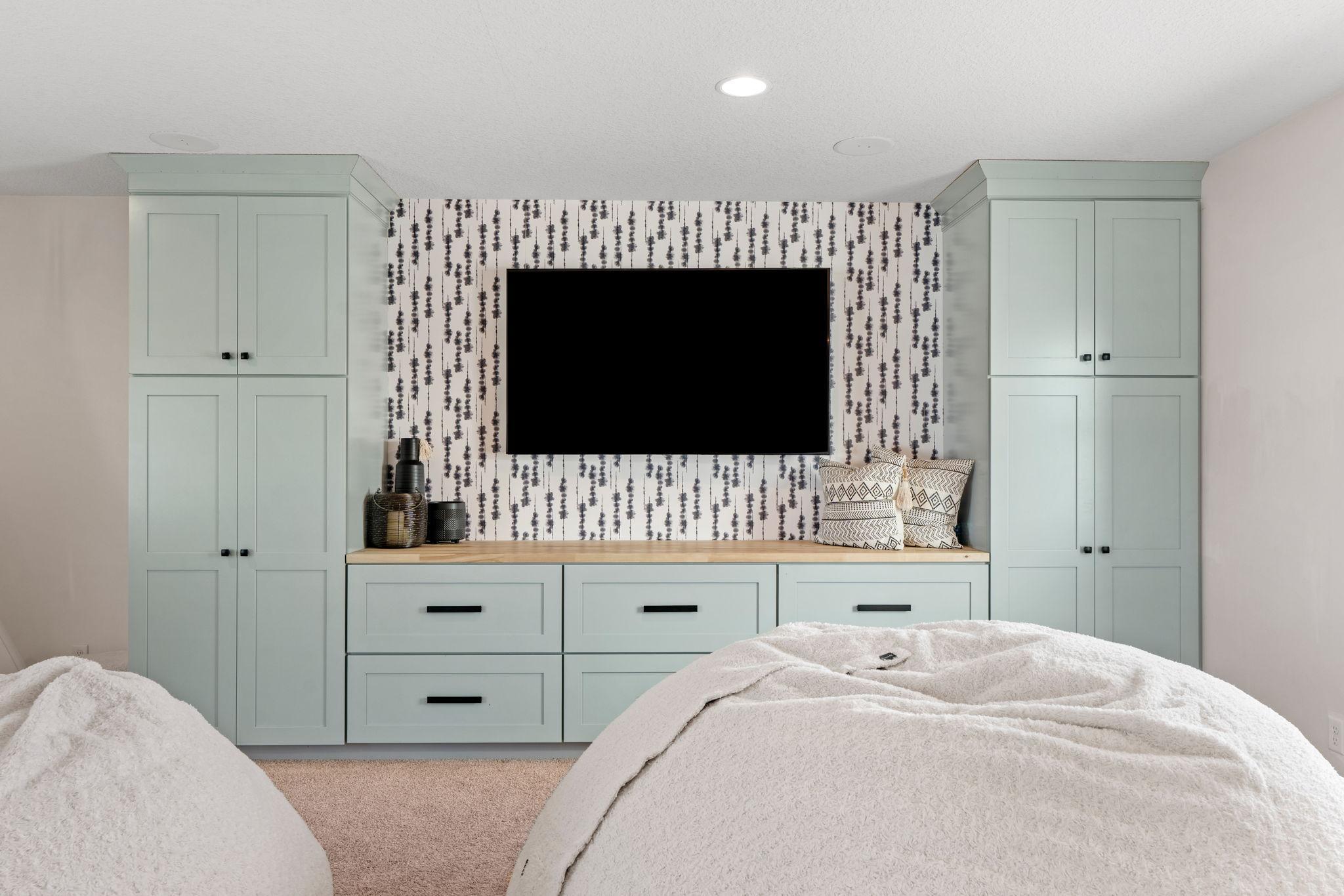 Bedroom with pale green built-in cabinets, a wall-mounted TV, and patterned wallpaper.
