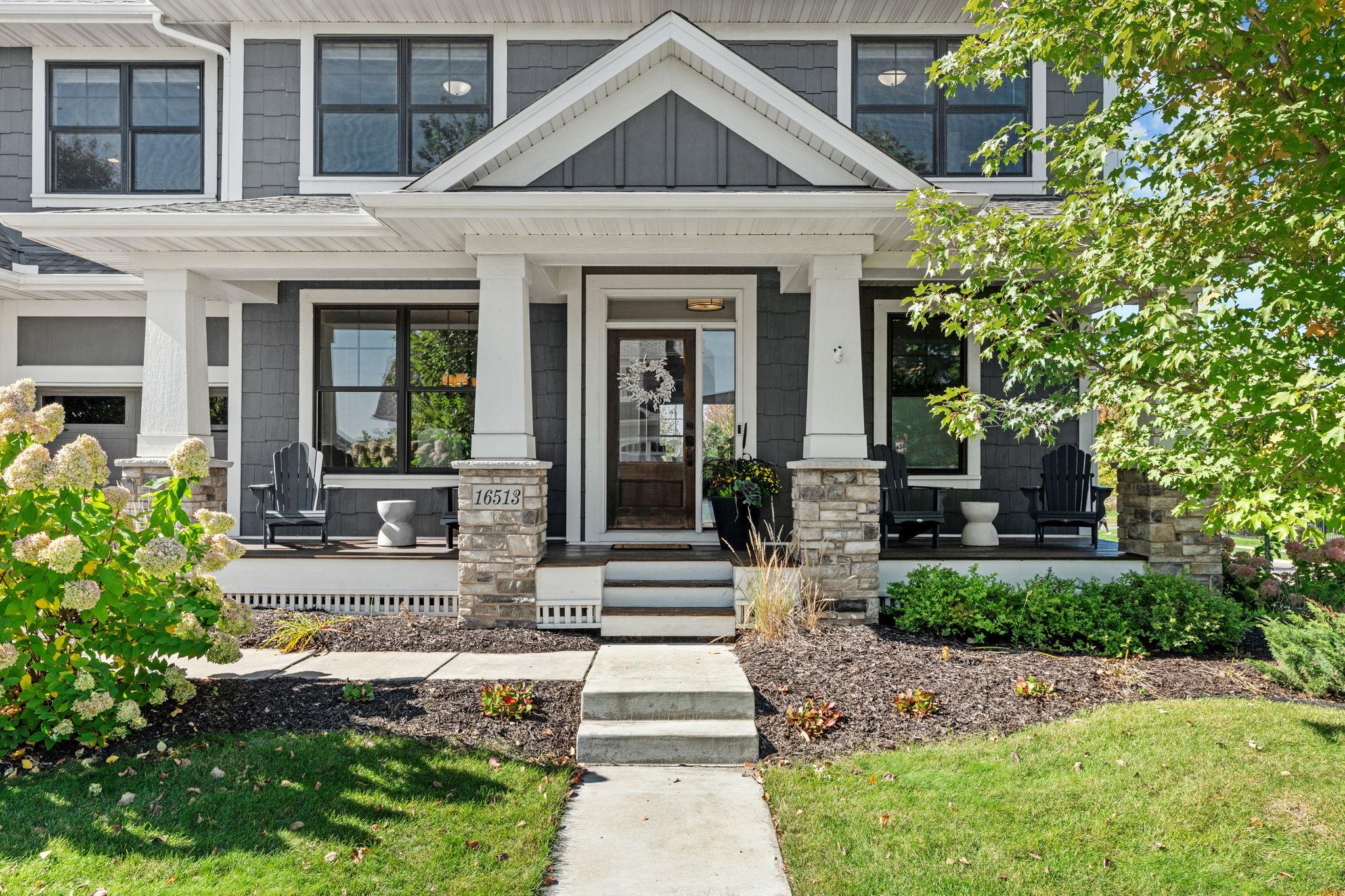 Two-story gray home with a covered porch, stone columns, and a walkway to the front door.