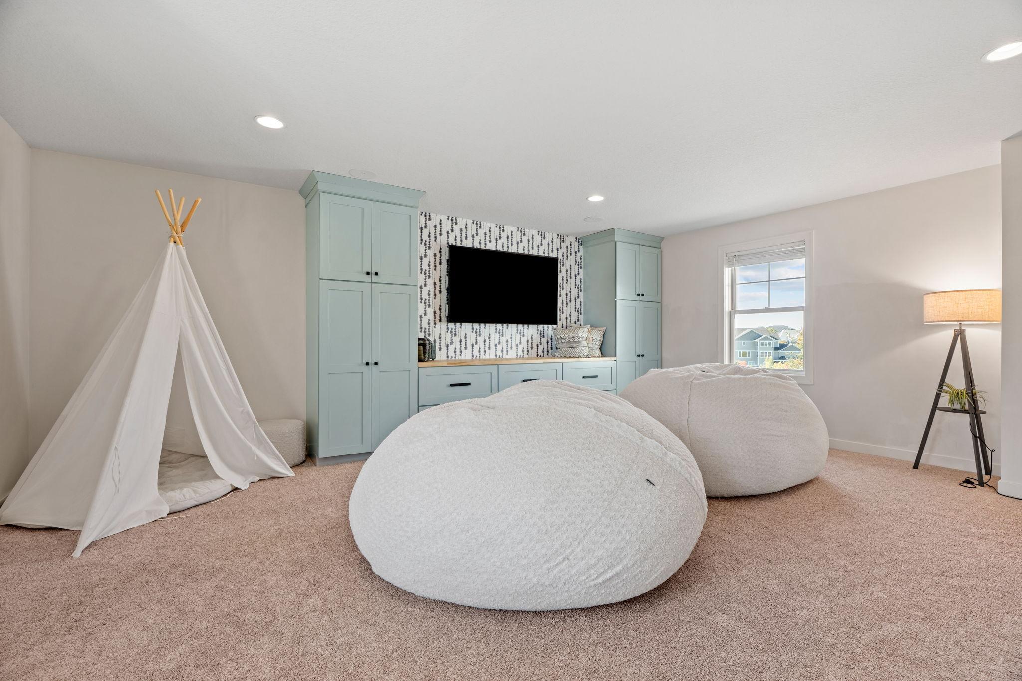 Playroom with pale blue built-ins, oversized beanbag chairs, and a white teepee.