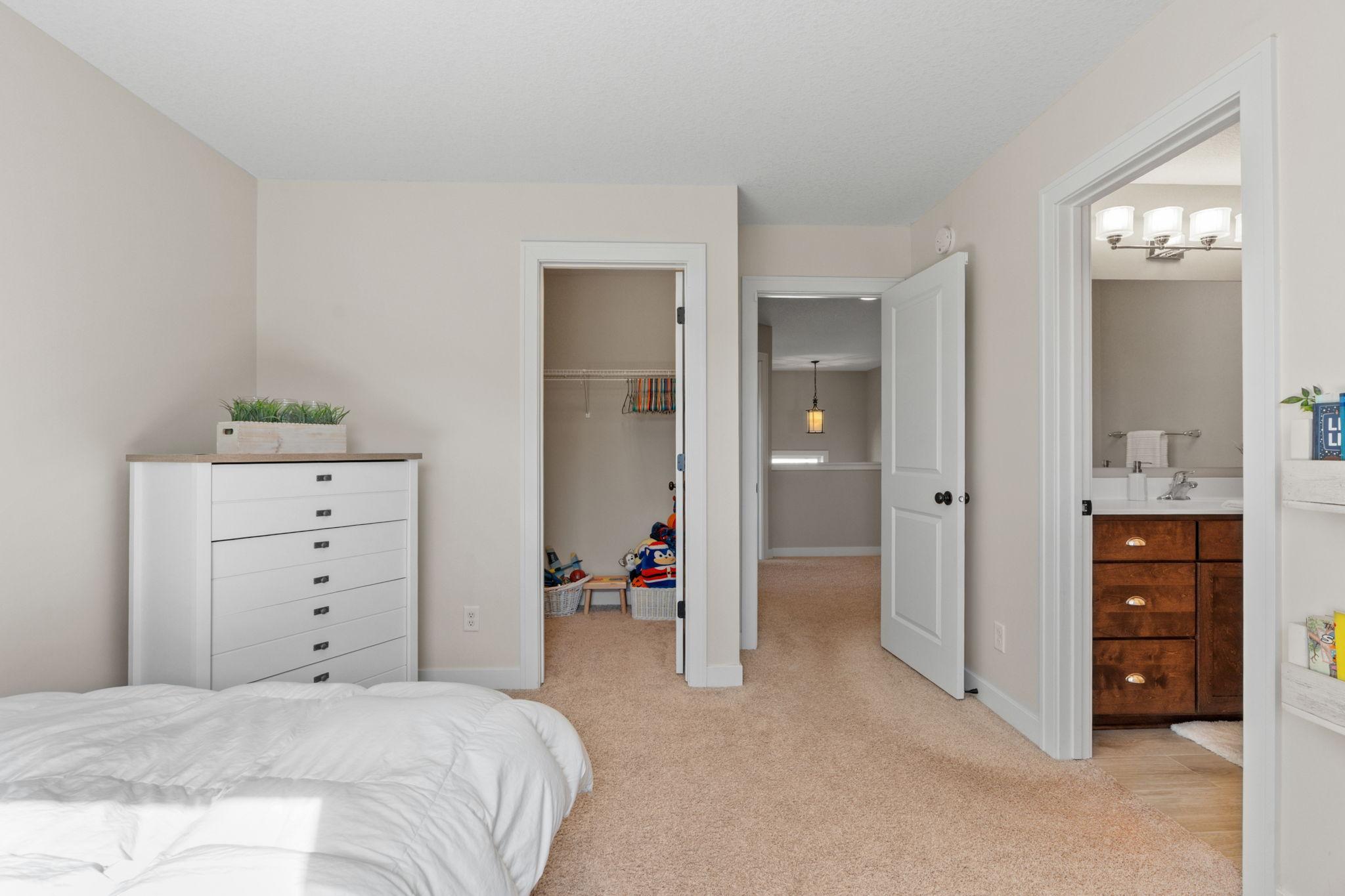 Bedroom with a white dresser, open toy closet, and doorway to an en-suite bathroom.
