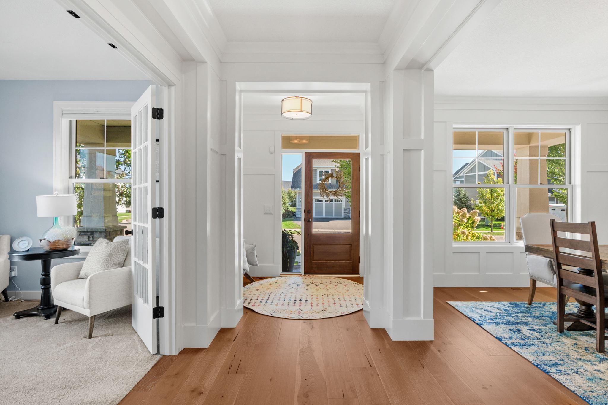 Bright entryway with a wood front door, hardwood floors, and views into adjoining sitting and dining areas.