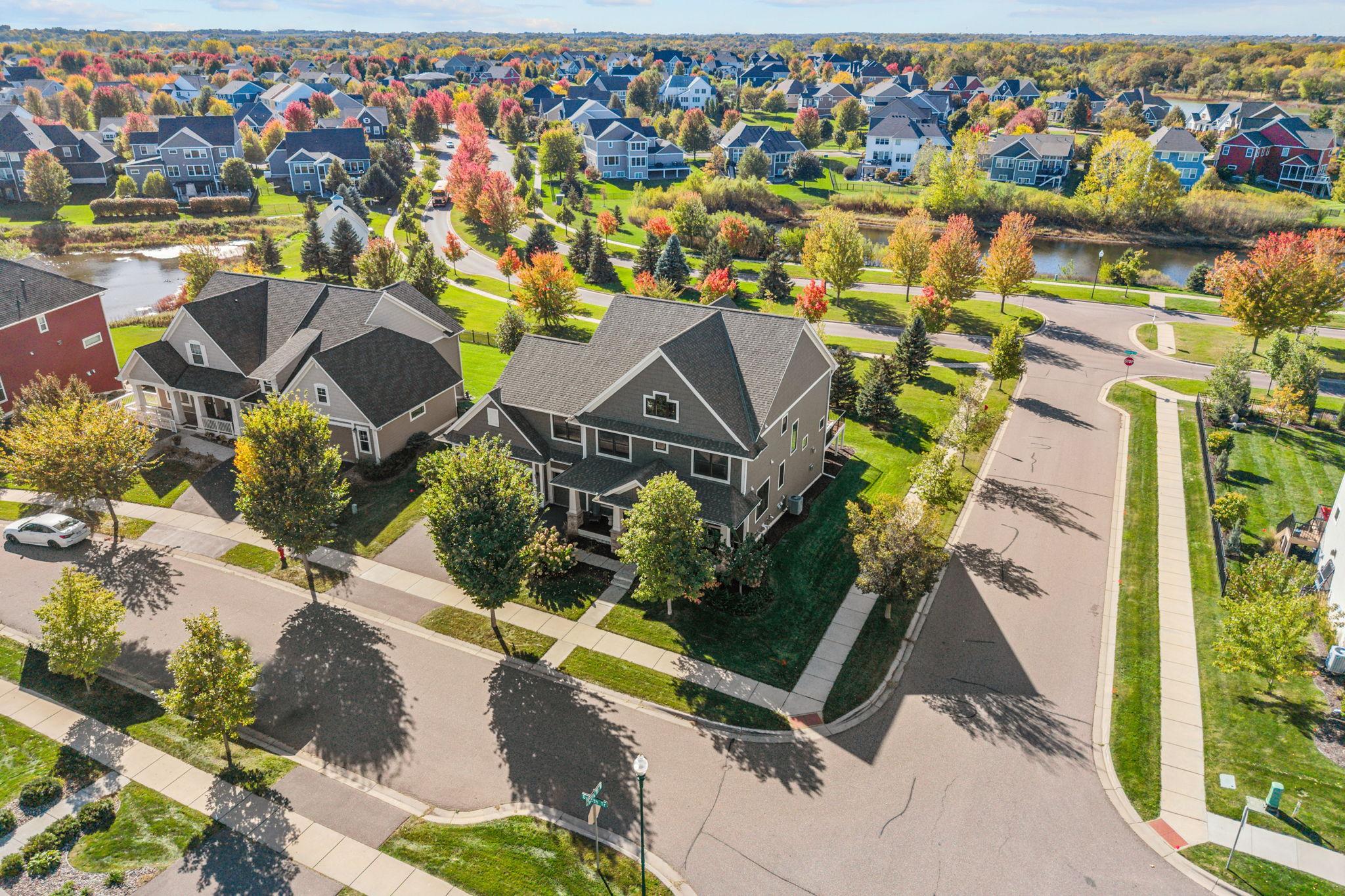 Aerial view of a gray two-story corner-lot home, with autumn trees and a pond nearby.