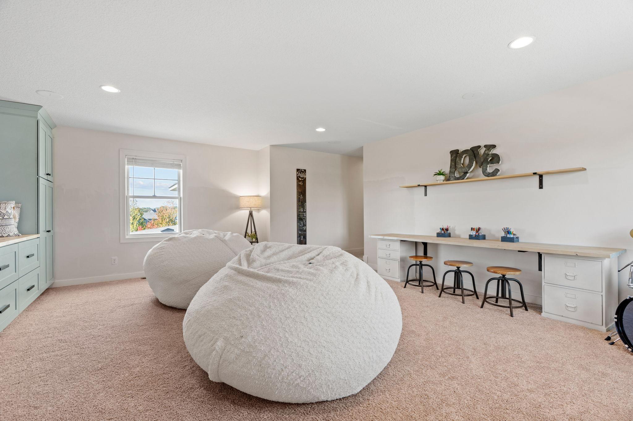 Furnished bedroom with oversized white beanbag chairs and a long desk with stools.