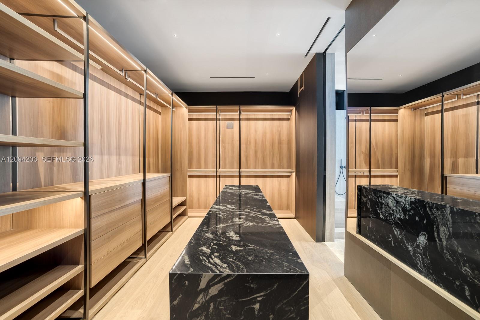 Walk-in closet with wood built-ins and a long black marble island.