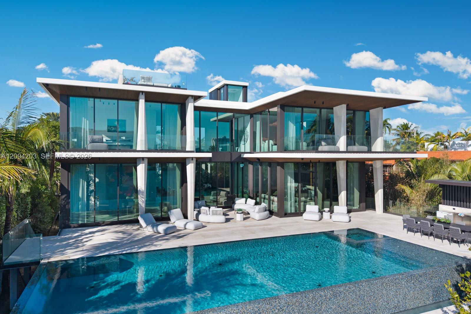 Modern glass house with angular rooflines, furnished terrace, and swimming pool.