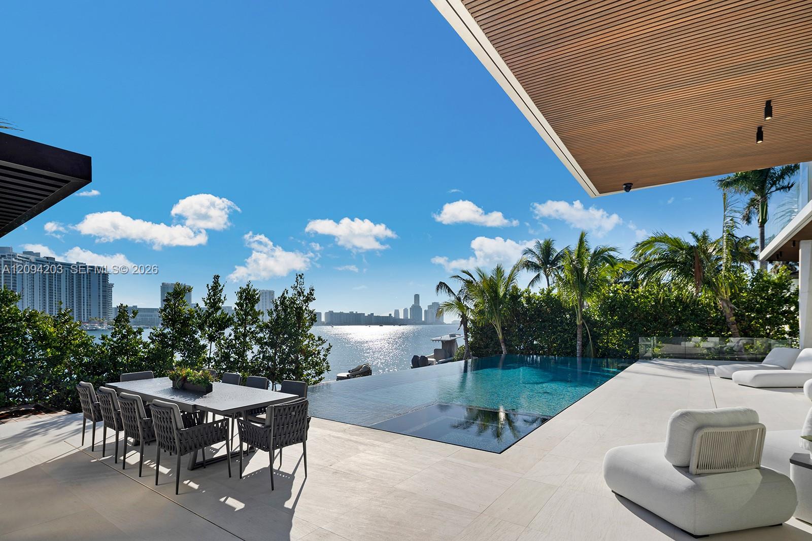 Waterfront terrace with infinity pool, outdoor dining area, and bay views toward the city skyline.