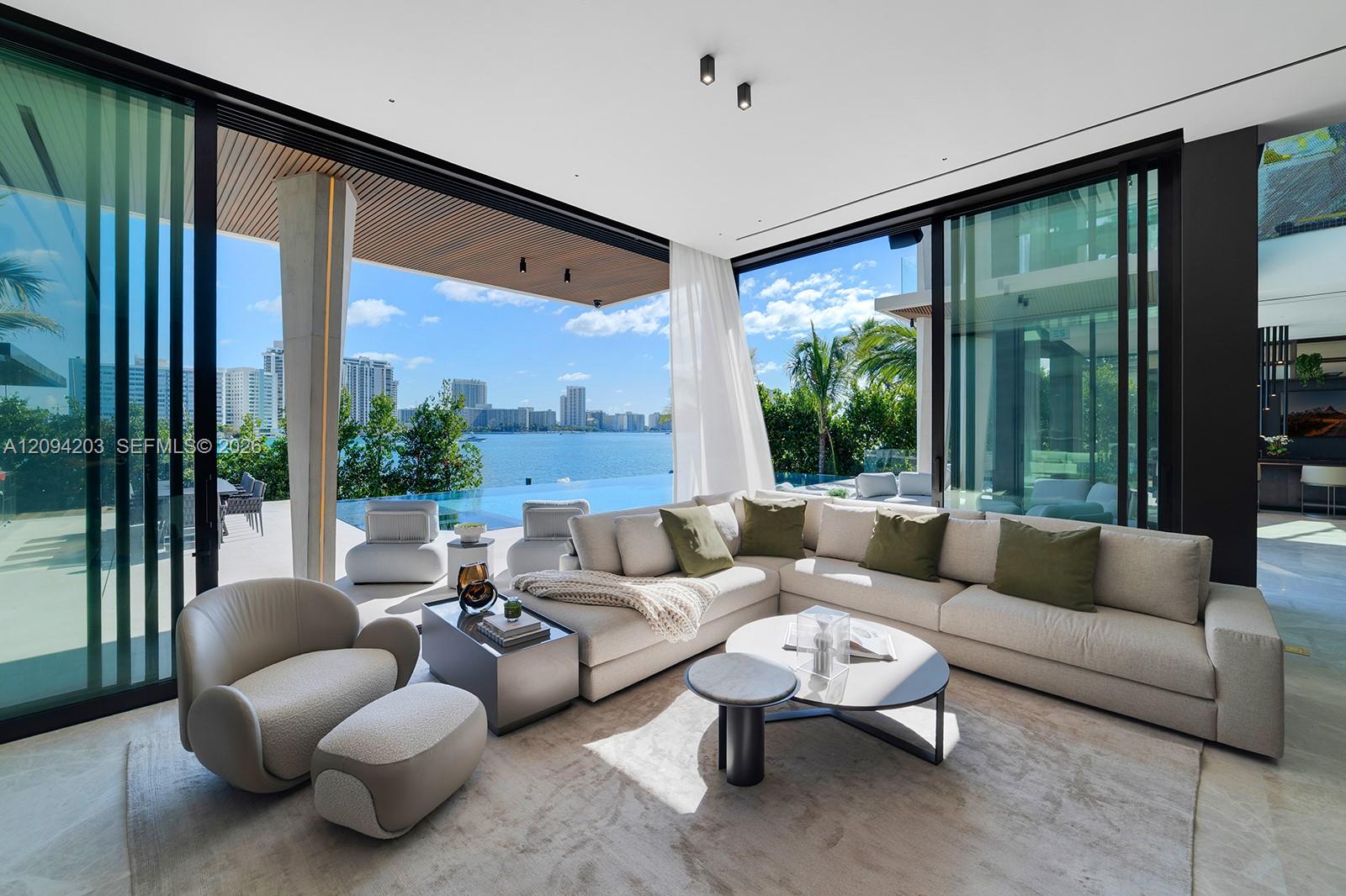 Modern living room with a large sectional, opening to a terrace and infinity pool overlooking the water.