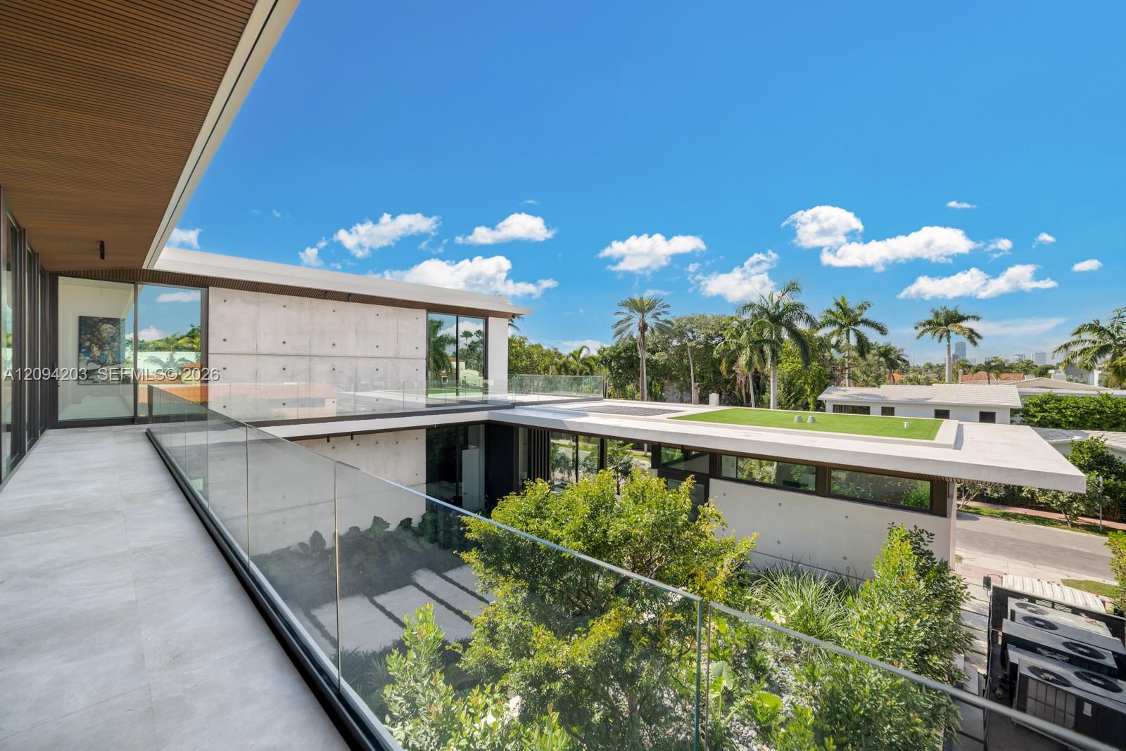 Modern concrete home with a glass-railed terrace overlooking landscaped grounds.