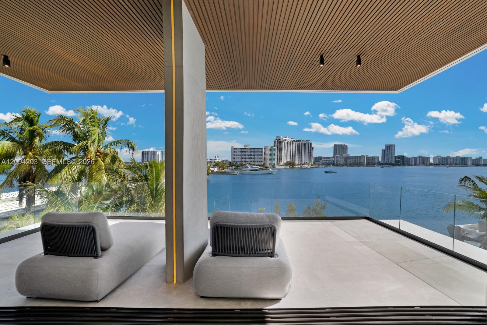 Covered waterfront terrace with sculptural lounge chairs overlooking open water and Miami Beach high-rises.