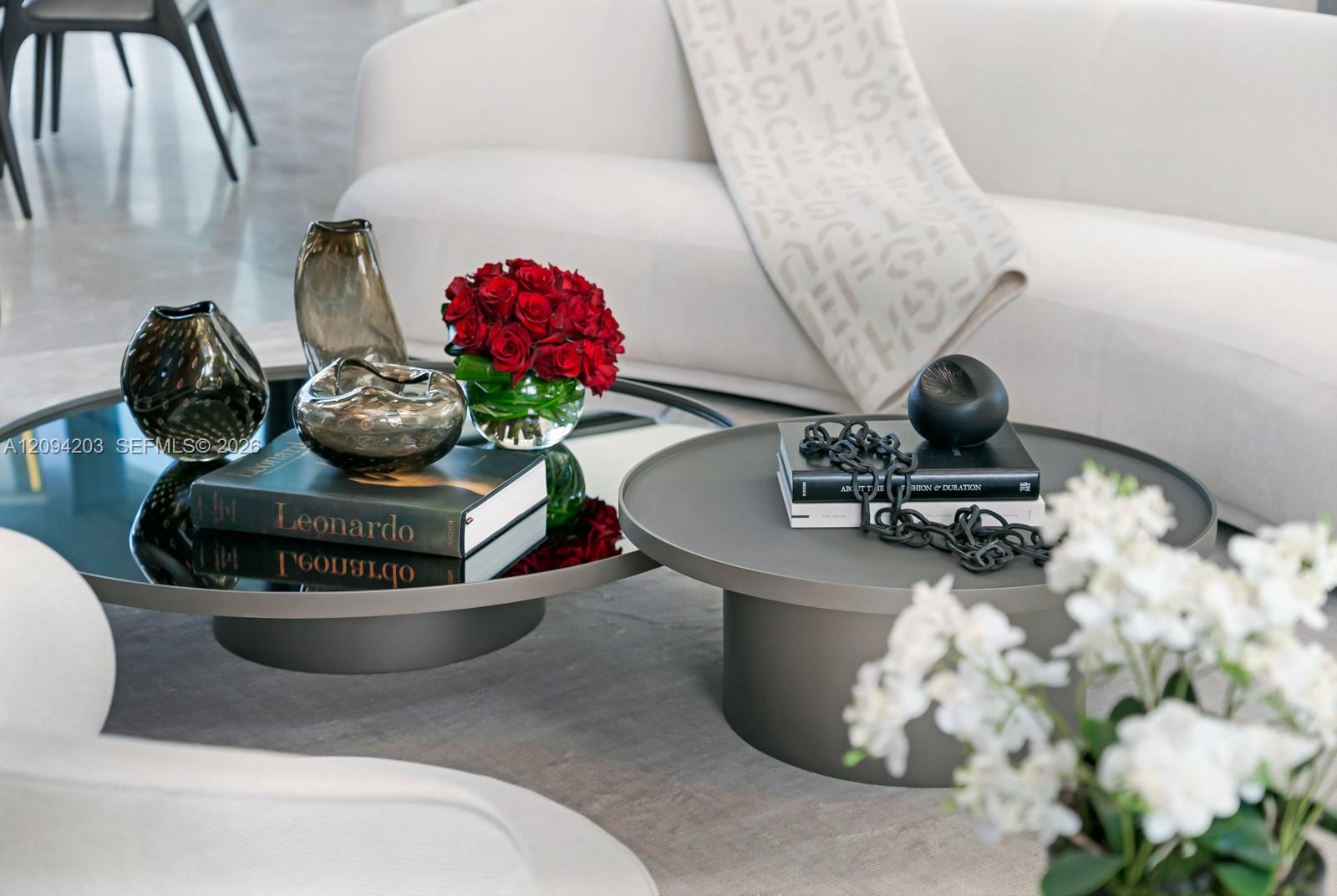 Living room seating and round coffee tables styled with red roses, decorative vases, and books.
