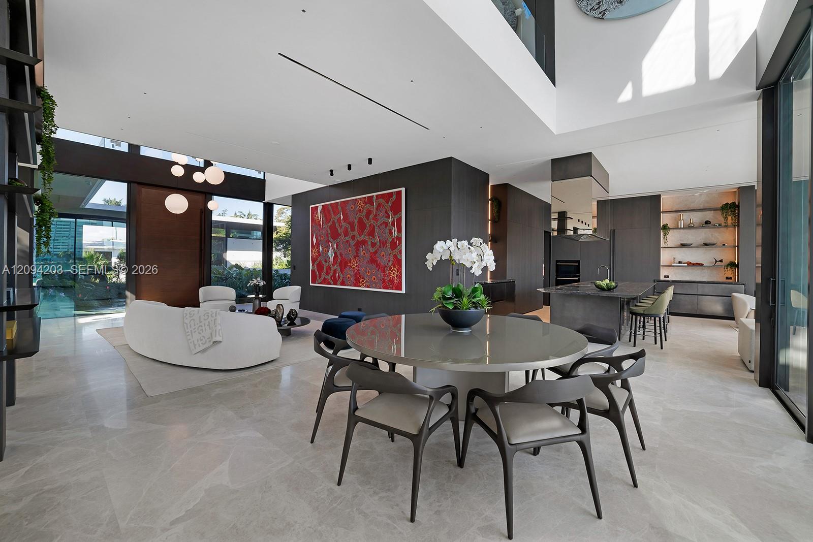 Open-plan dining and living area with a round table, white seating, and a modern kitchen.