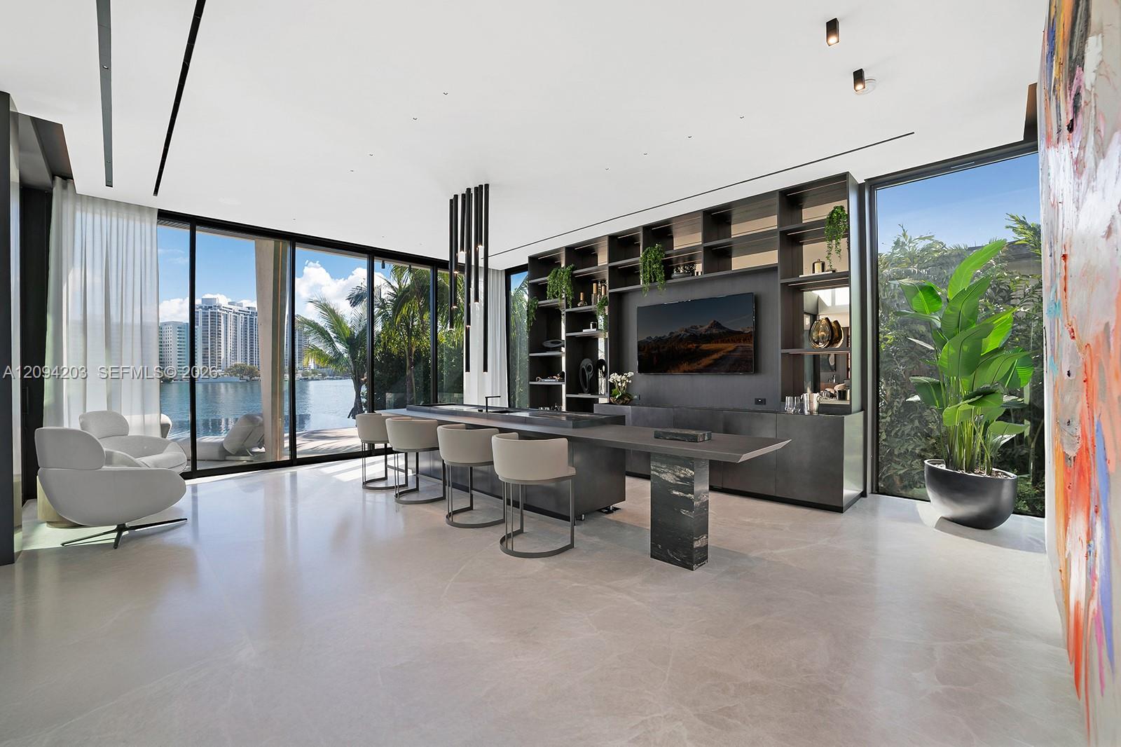 Modern living room with a kitchen island and water views through floor-to-ceiling windows.