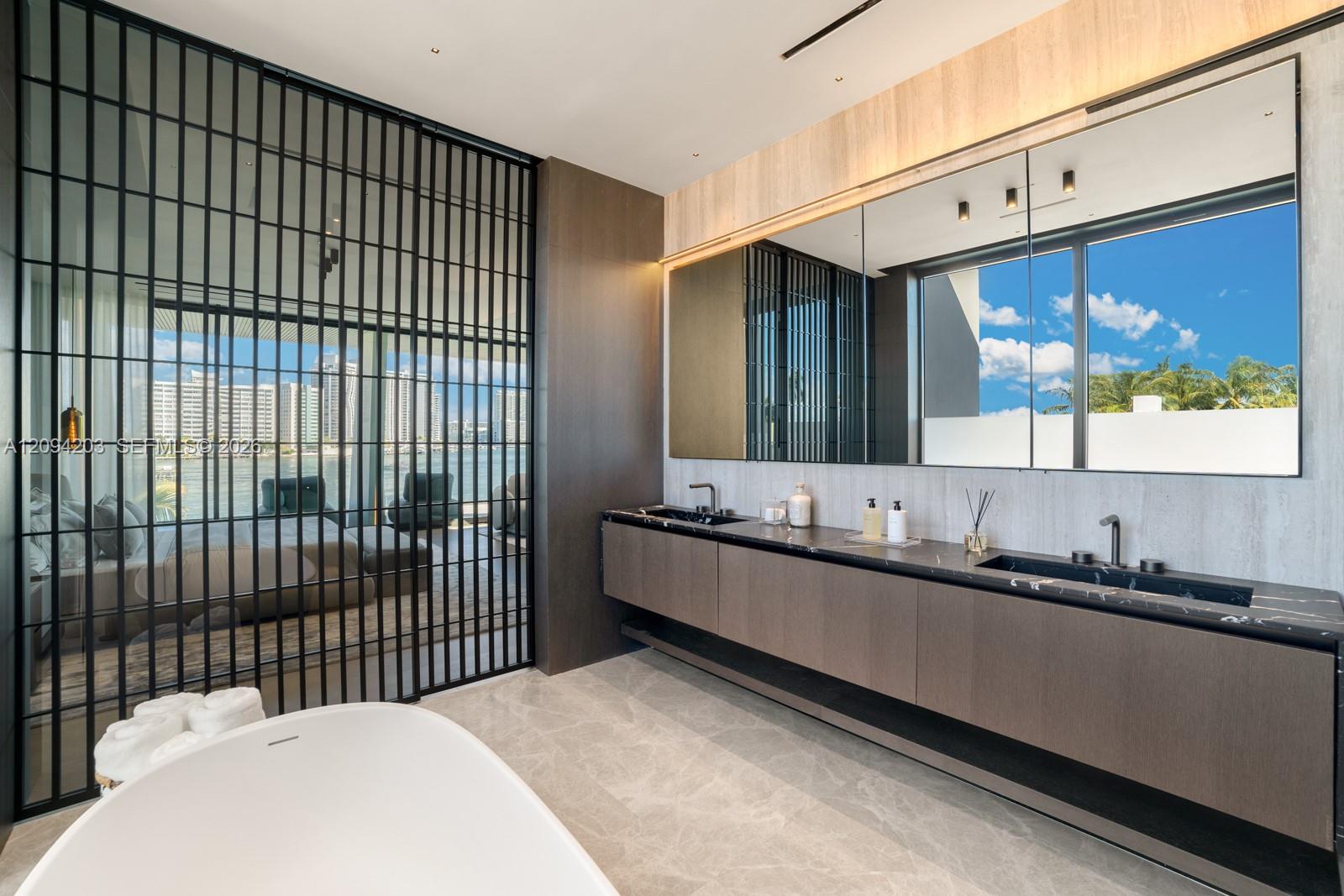 Modern bathroom with a freestanding tub, dark double vanity, and views of water and high-rises.