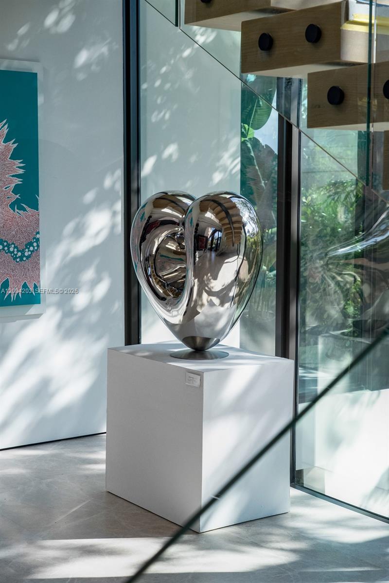 Polished silver heart sculpture on a white pedestal beside floor-to-ceiling glass walls.