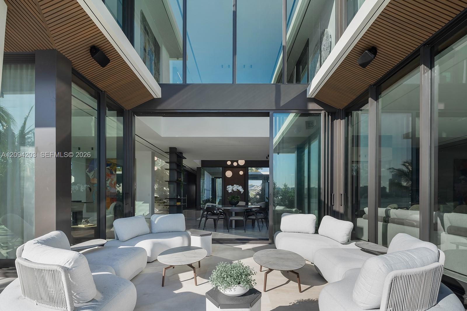 Modern patio with white lounge seating, round tables, and floor-to-ceiling glass doors.