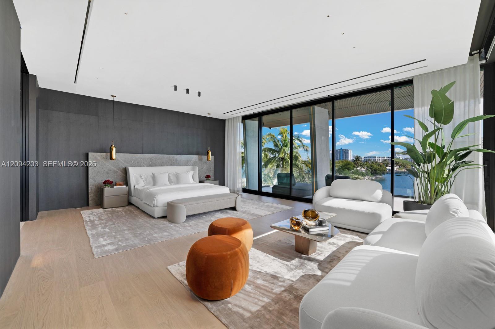 Modern bedroom suite with a sitting area and floor-to-ceiling windows overlooking the water.