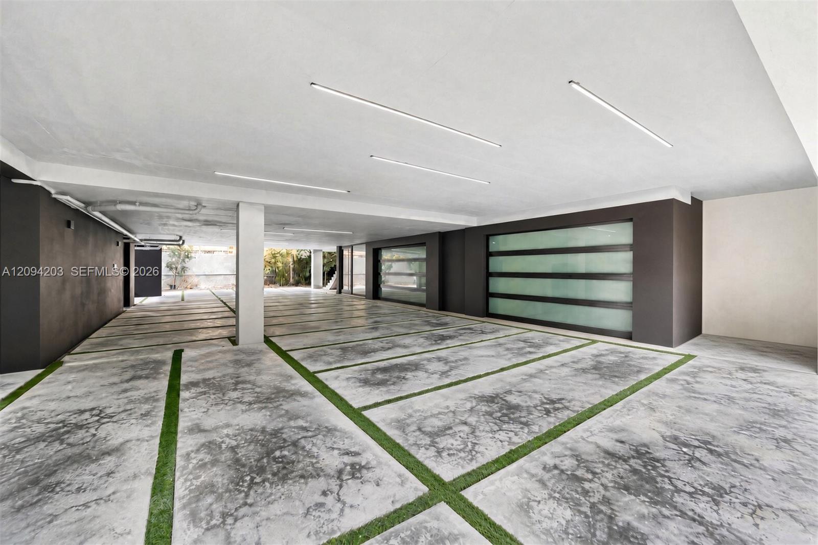 Covered garage with concrete parking bays divided by grass strips and wide frosted-glass doors.