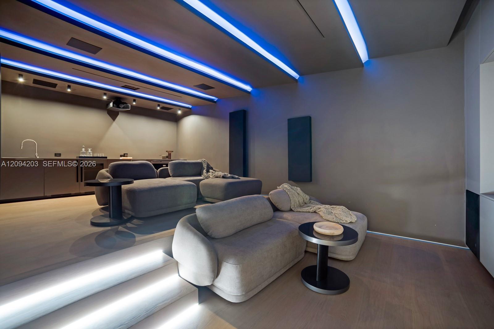Home theater with tiered lounge seating, illuminated steps, and blue ceiling lighting.