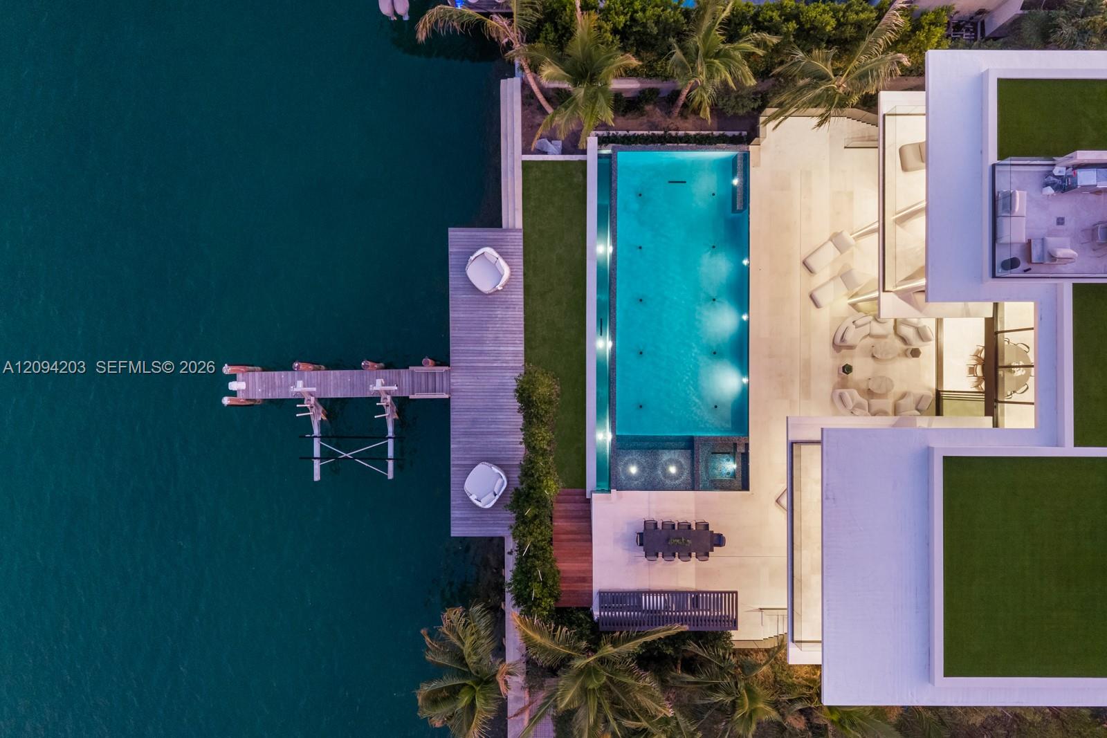 Waterfront home with an illuminated pool, landscaped terraces, and a dock extending over the water.