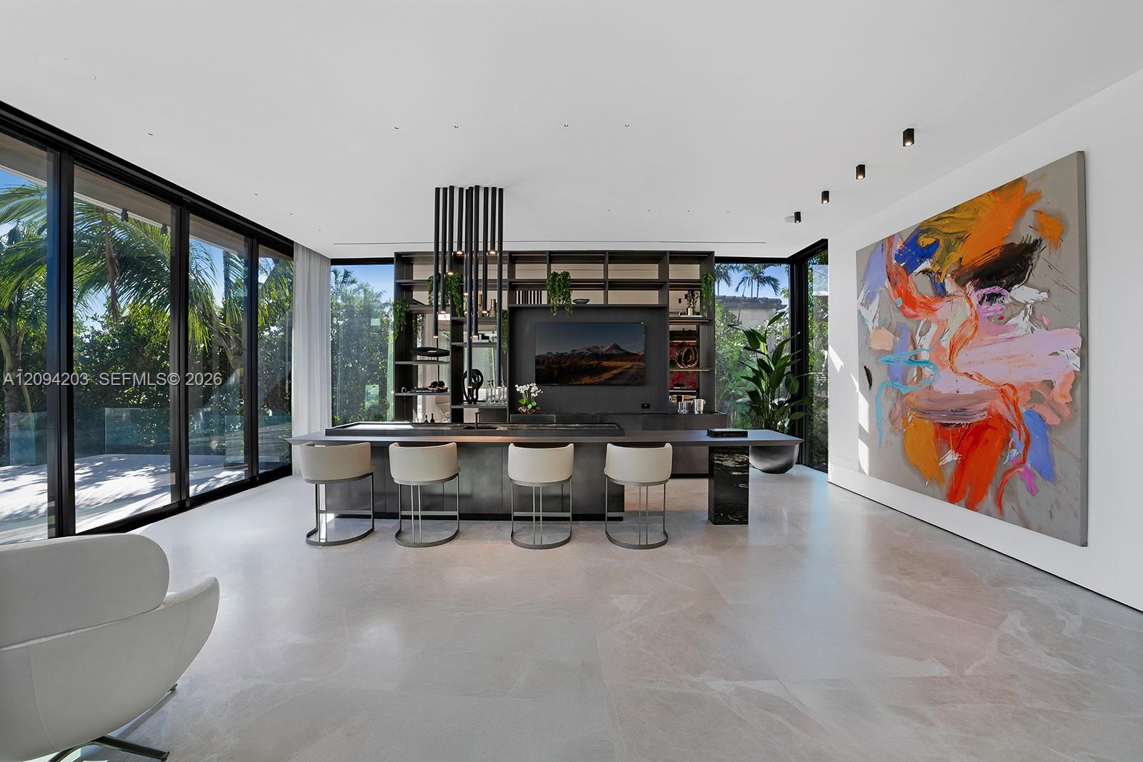 Contemporary kitchen with a dark island, four white stools, floor-to-ceiling windows, and a large colorful painting.
