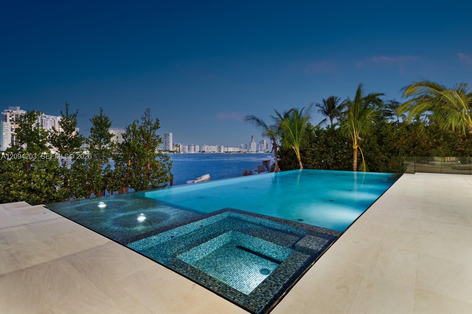Waterfront pool and tiled spa overlook the bay and Miami skyline, framed by palm trees.