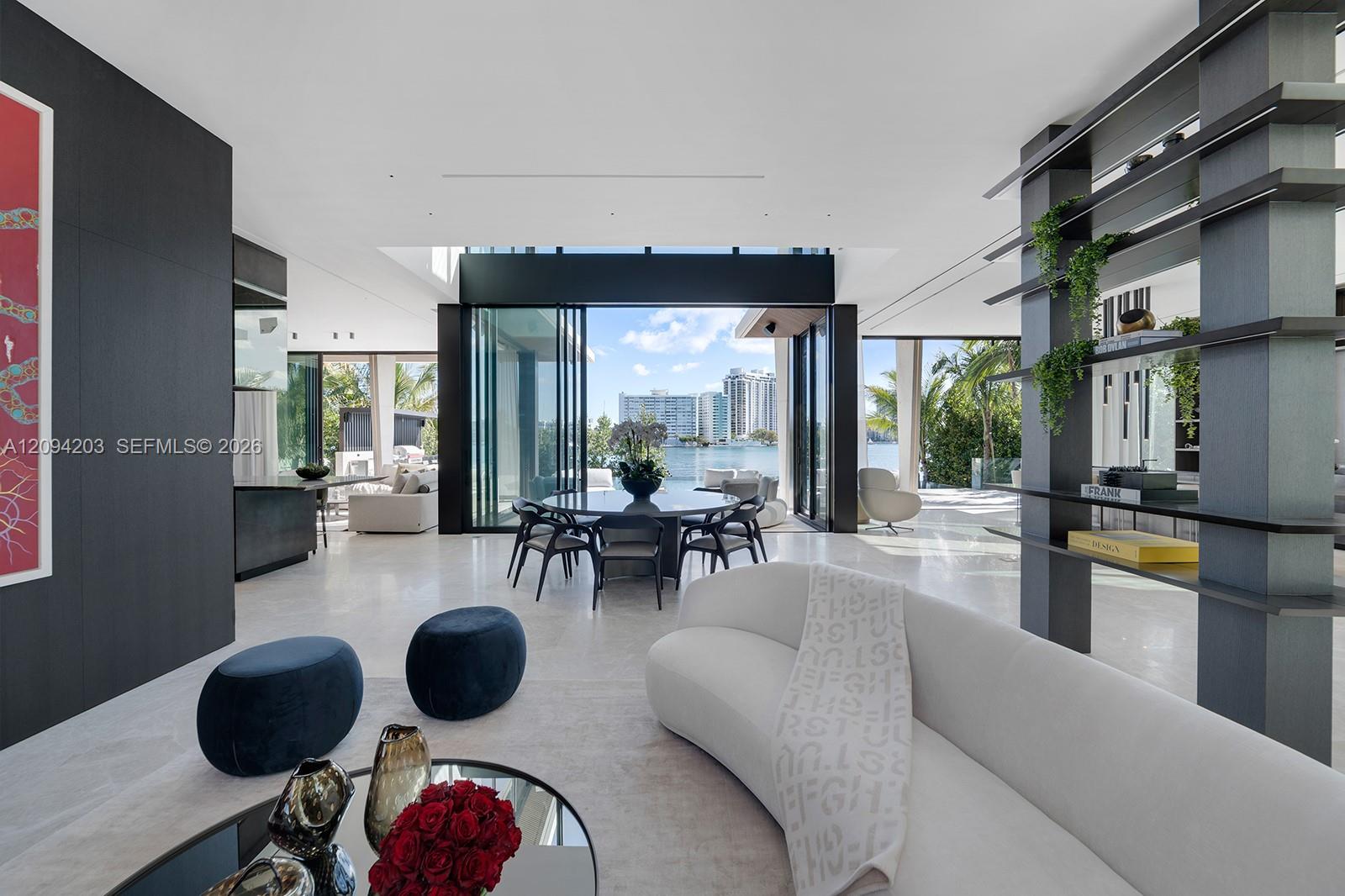 Modern living and dining room with floor-to-ceiling glass doors and a waterfront view.