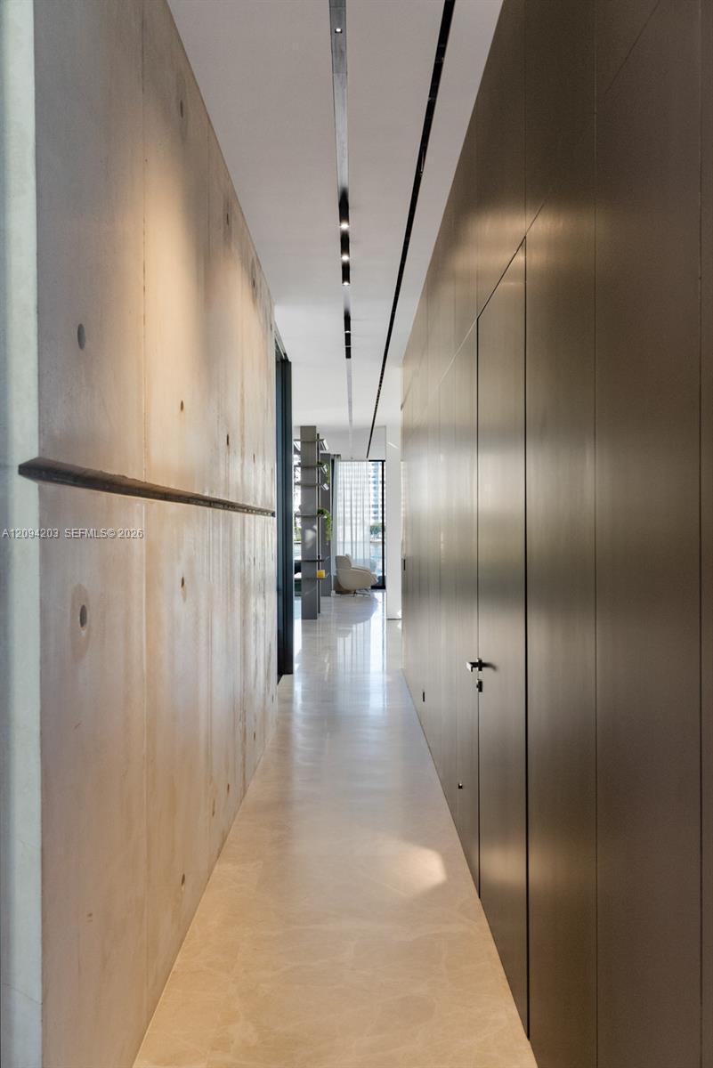 Modern hallway with pale stone flooring, wood paneling, and dark flush cabinetry.