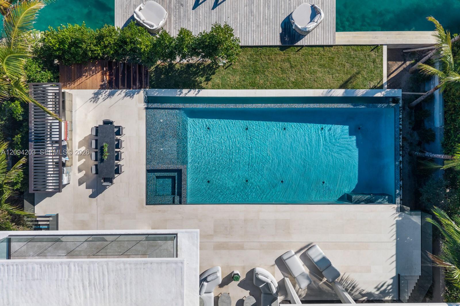 Aerial view of a modern swimming pool with a sun shelf, built-in spa, and furnished patio.