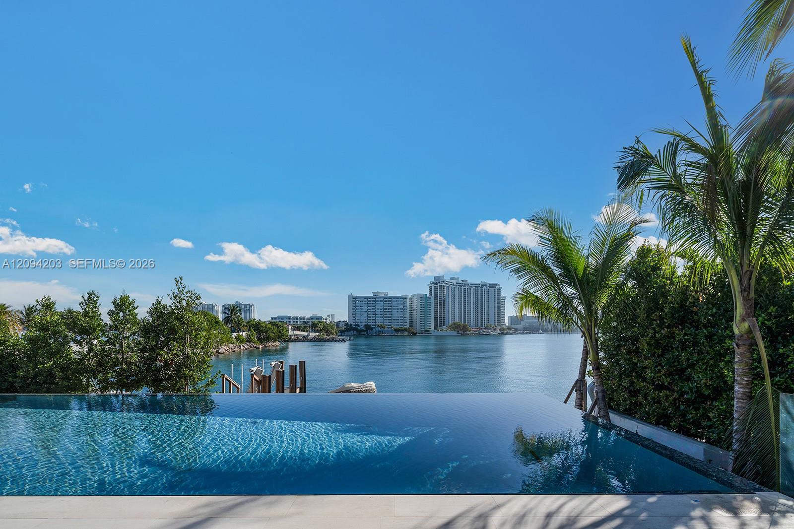 Infinity pool overlooking a waterway, framed by palm trees with high-rises across the water.