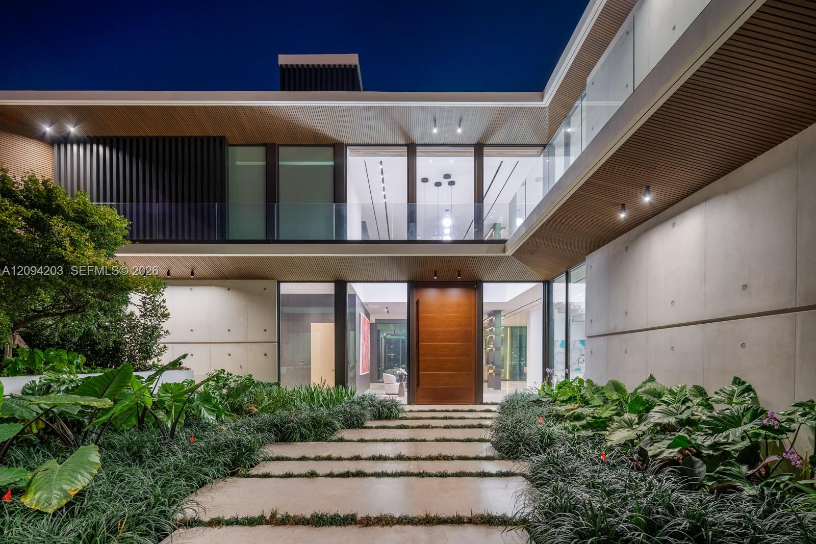 Modern home entrance framed by tropical landscaping, with an oversized wood door and glass facade.