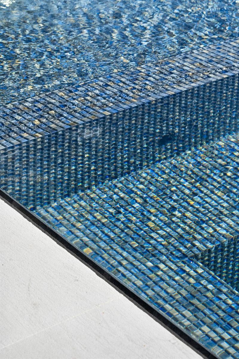 Pool water ripples over blue mosaic tiles beside a raised tiled edge and pale stone coping.