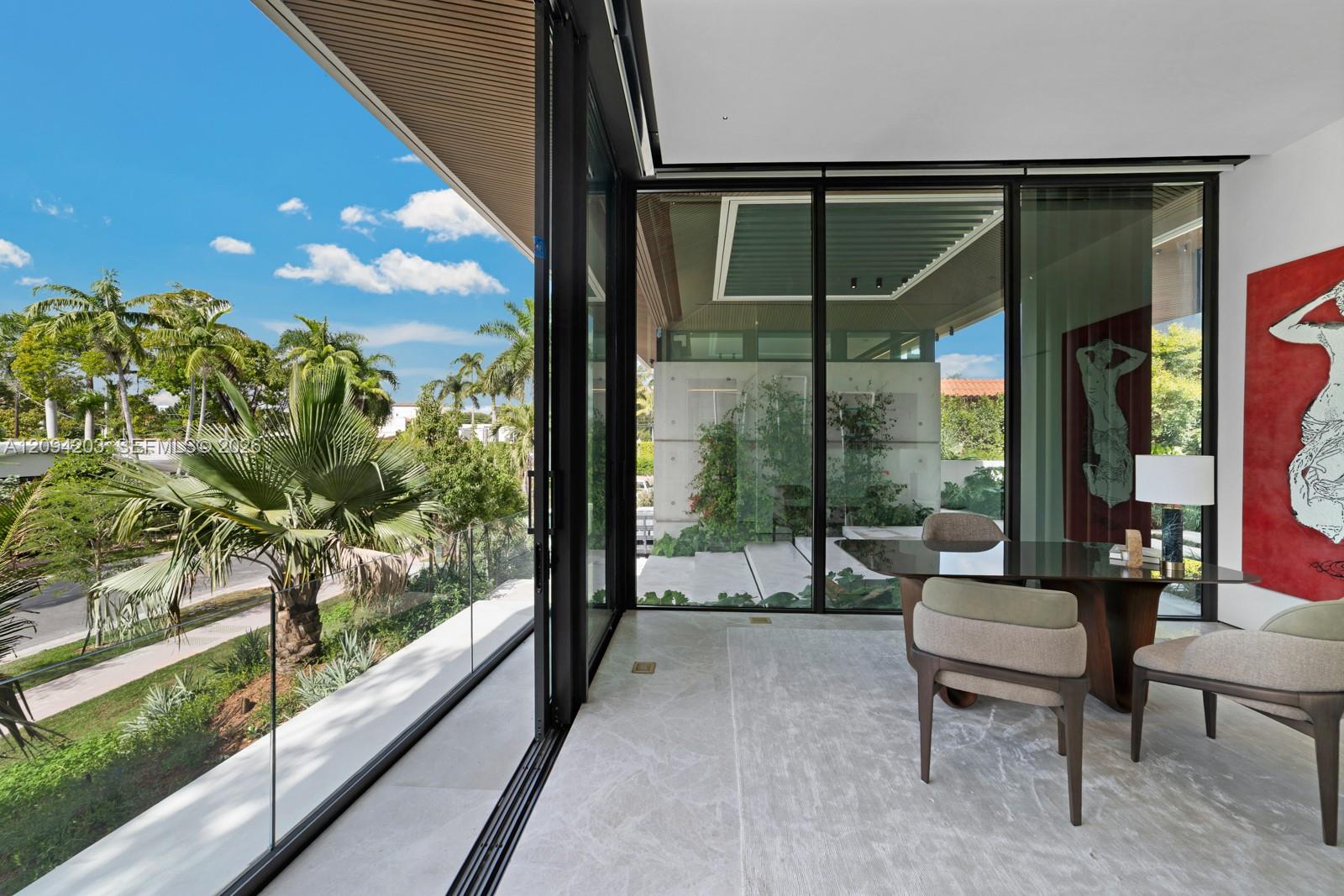 Dining area with floor-to-ceiling glass walls overlooking palm trees and a tropical garden.