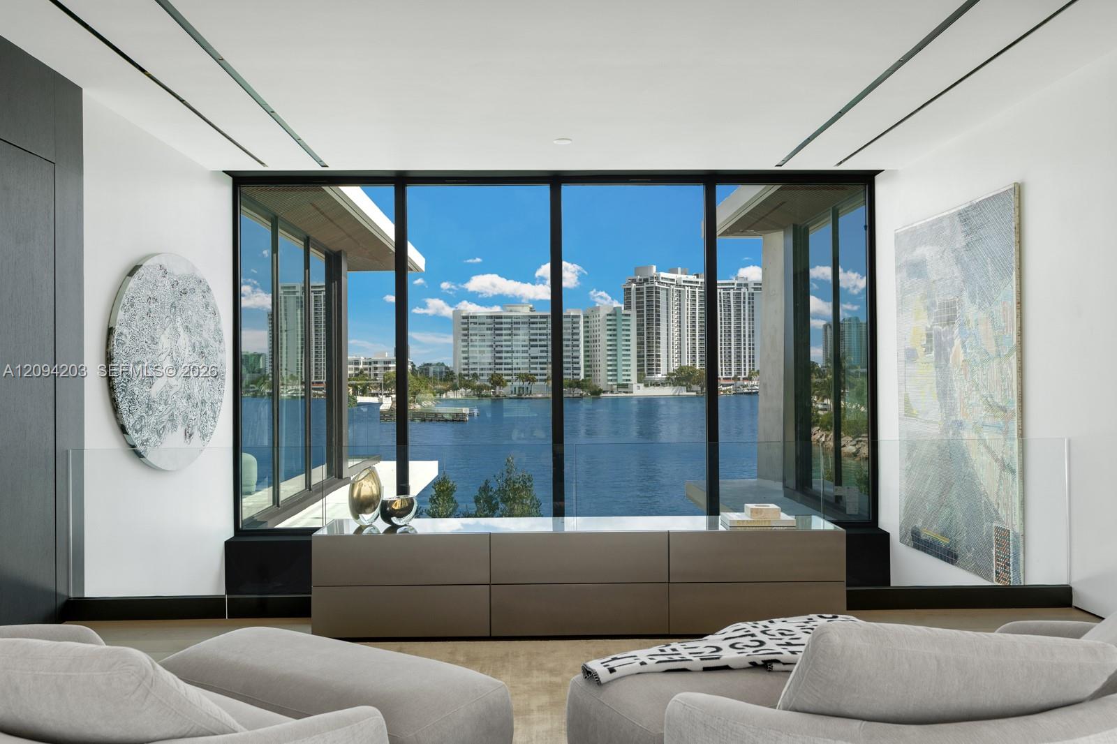 Modern living room with floor-to-ceiling windows overlooking water and a city skyline.