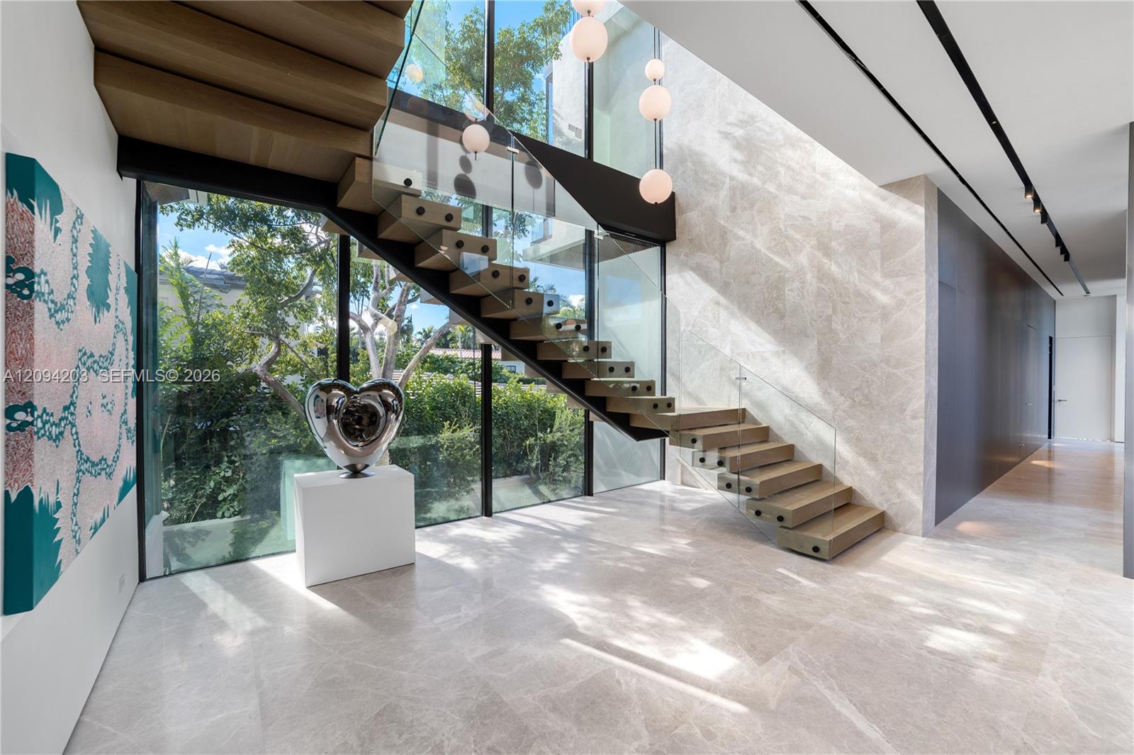 Modern foyer with a glass-railed staircase, marble floors, and floor-to-ceiling windows.