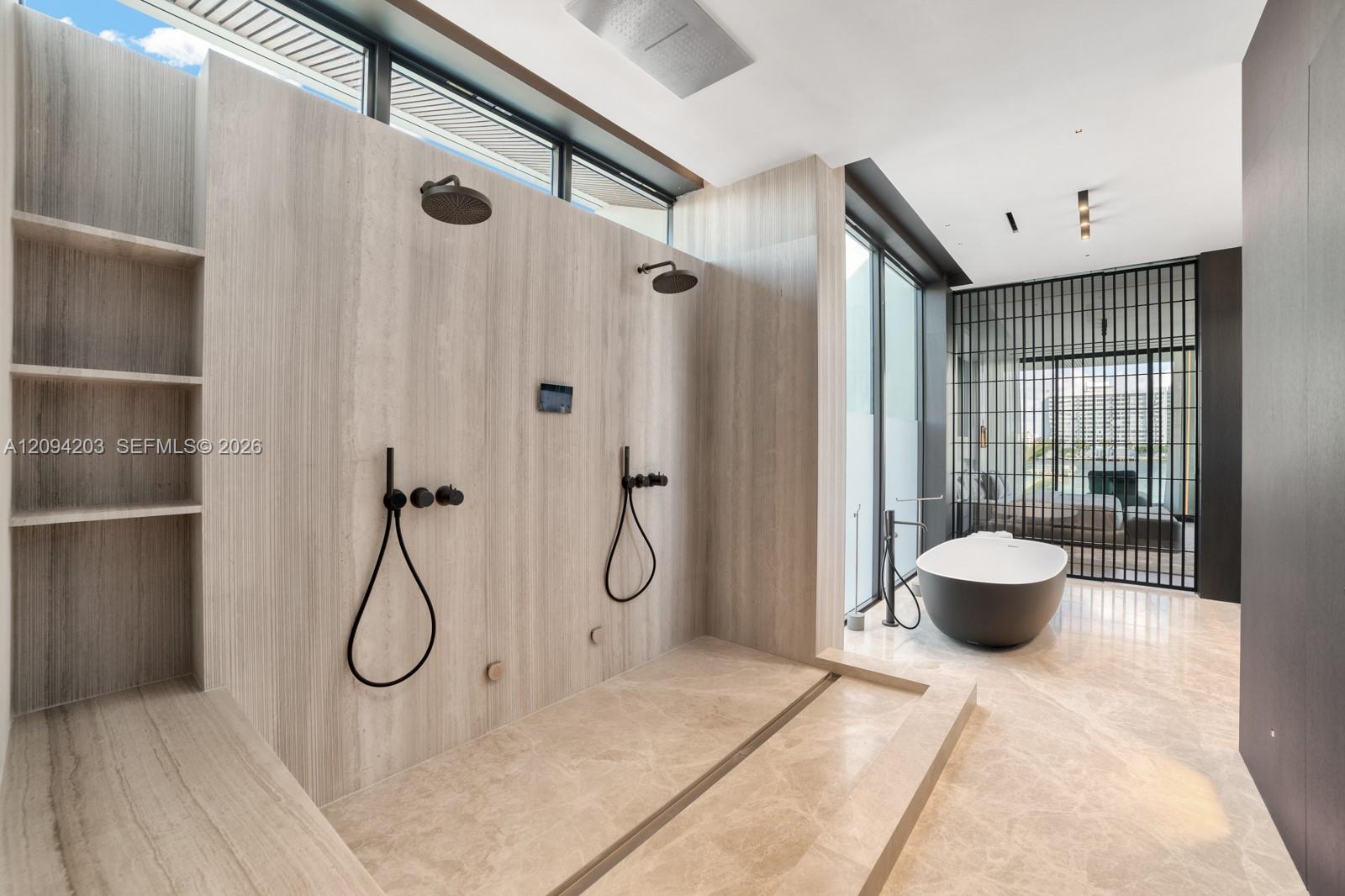 Modern stone bathroom with a spacious walk-in shower, black fixtures, and a freestanding tub beside a water view.