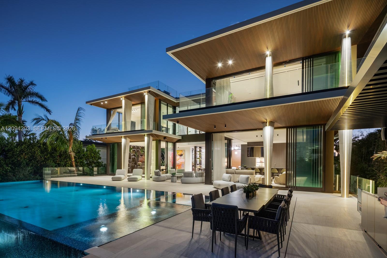 Modern glass home with a lit pool and outdoor dining terrace at dusk.
