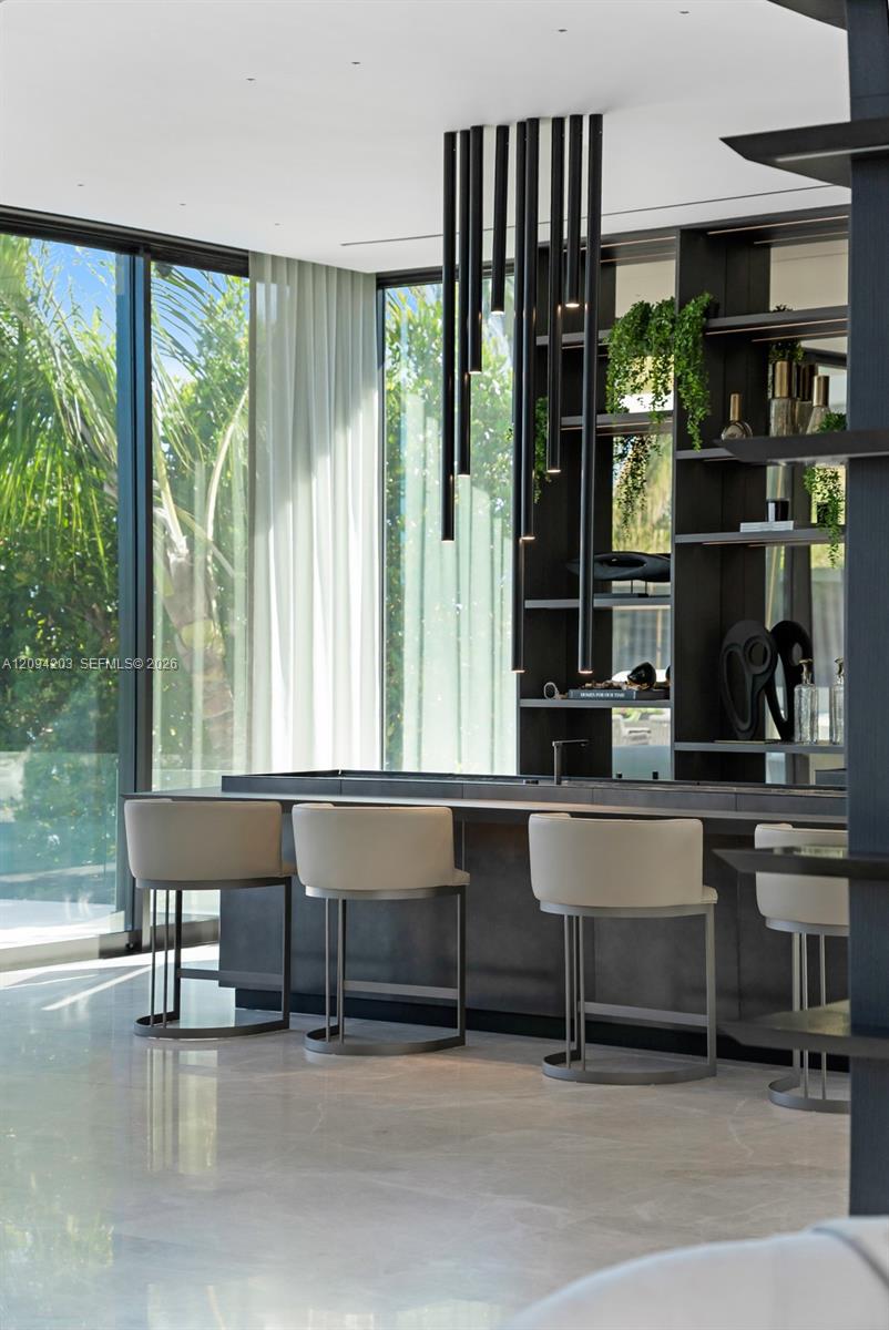 Modern kitchen with a dark island, pale bar stools, and floor-to-ceiling windows overlooking greenery.