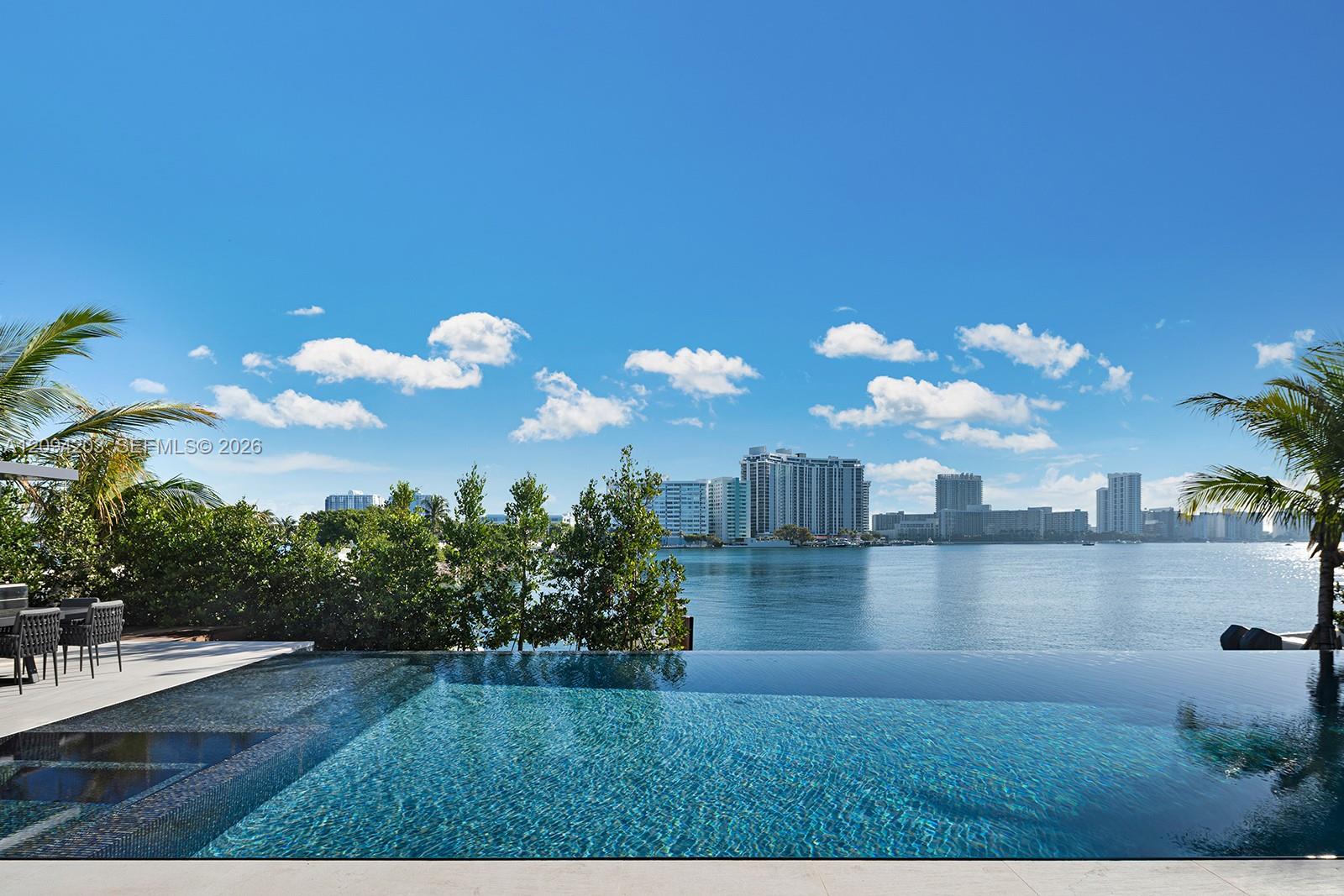 Infinity pool overlooking Biscayne Bay and Miami high-rises, framed by palms and an outdoor dining area.