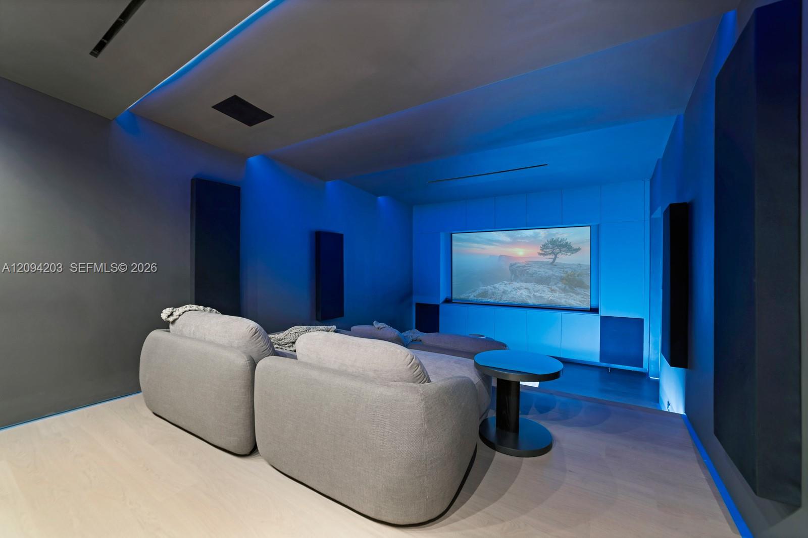 Home theater with gray sectional seating, a large screen, and vivid blue accent lighting.