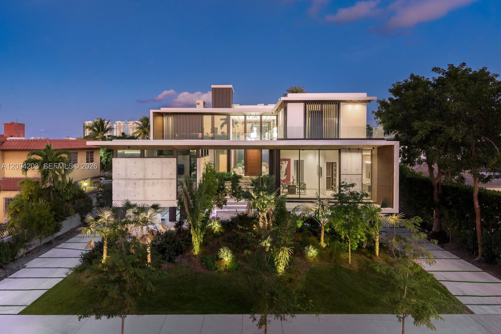 Modern two-story home with glass walls and landscaped grounds at dusk.