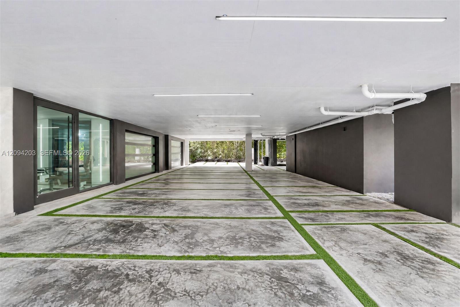 Covered parking area with concrete bays divided by strips of grass beside modern glass doors.