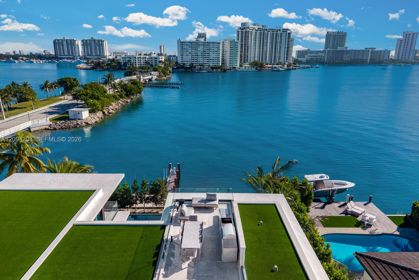 Aerial view of a waterfront home with rooftop terraces, pool, boat dock, and bay skyline.